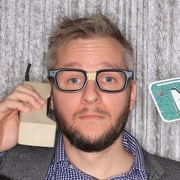 Chris Katzer holding a 1980s brick mobile phone to his ear.